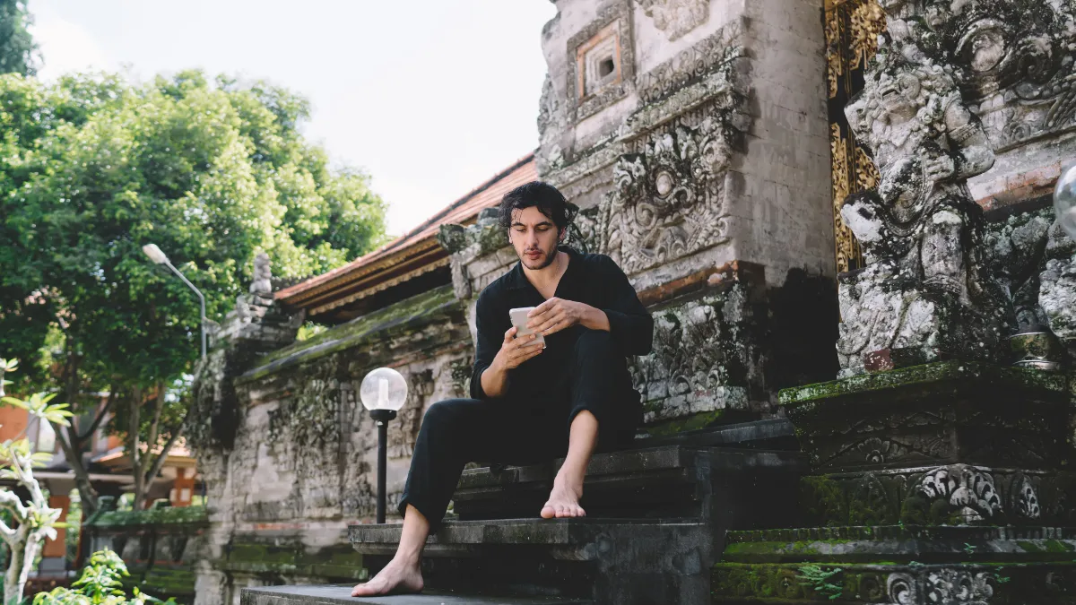 Escaping heat to use mobile phone at temple in Bali - essential gear for solo travelers