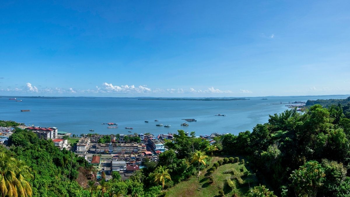 Panoramic view of Sandakan a coastal town, boats on a calm bay, lush hills, and blue sky