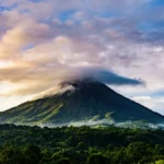Volcanic mountain rising above a lush green forest under a cloudy sky