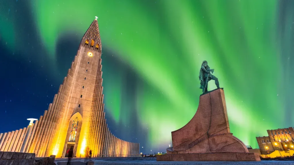 Aurora borealis over a lit church and statue at night