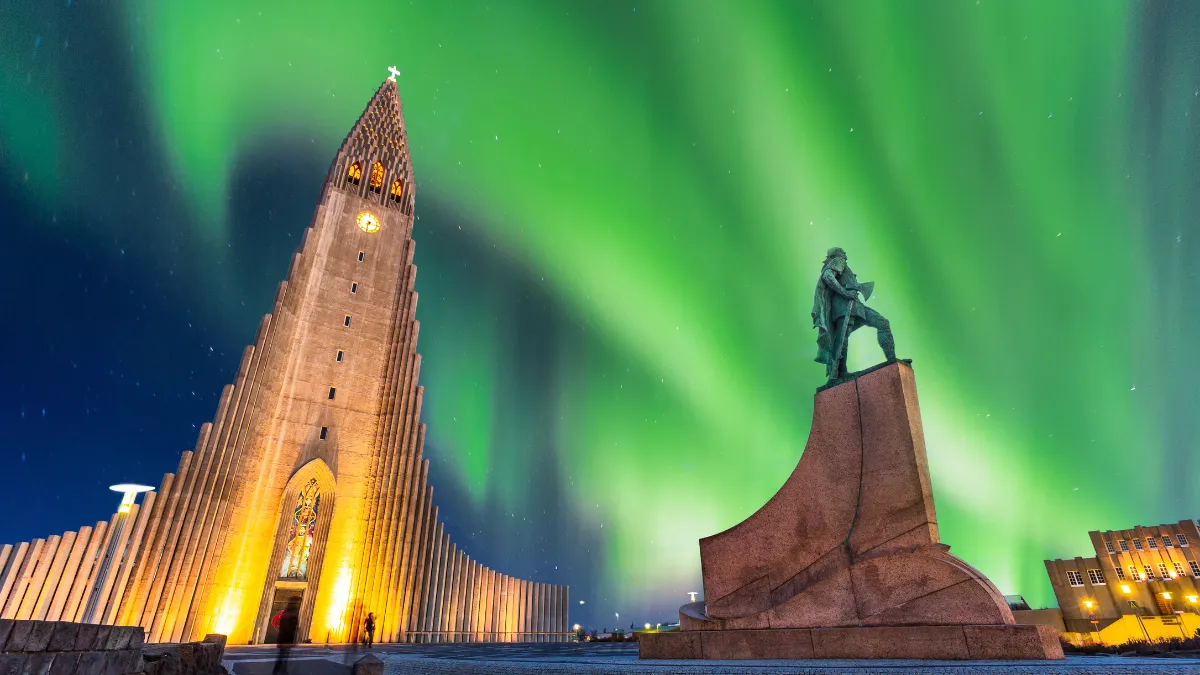 Aurora borealis over a lit church and statue at night