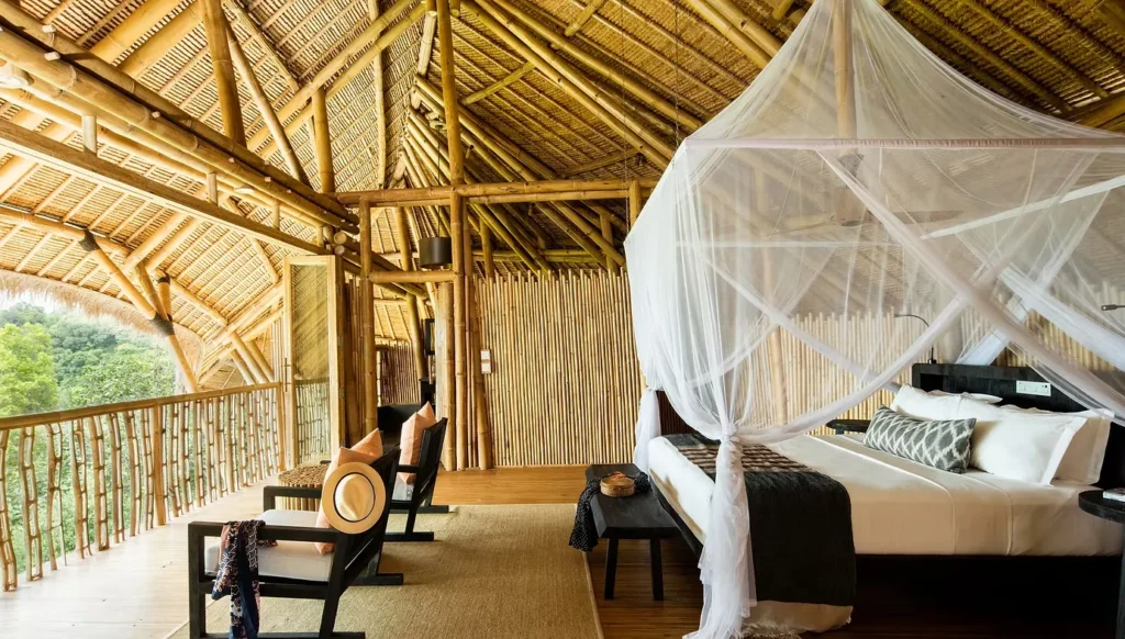 Open-air bamboo resort bedroom with a canopy bed and balcony seating
