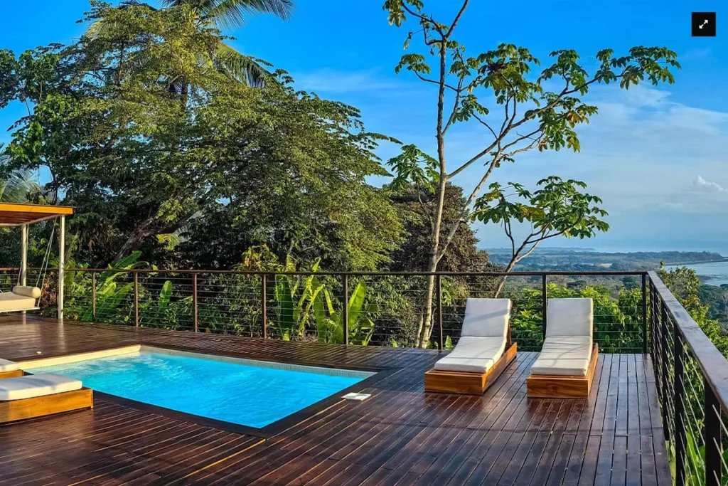 Tropical deck with a small pool, lounge chairs, and a view of the ocean and forest
