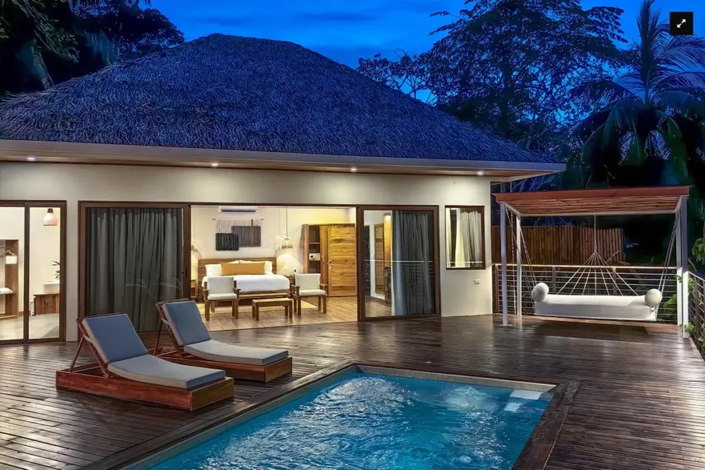 Private villa deck with a small pool, lounge chairs, and a hanging daybed at dusk