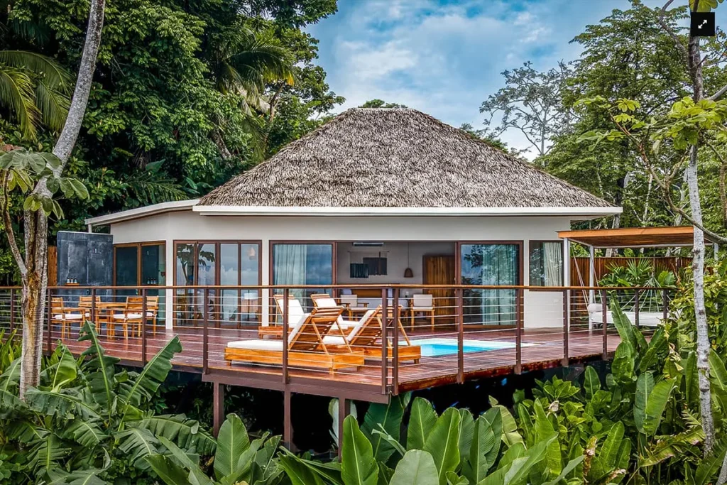 Tropical villa with a thatched roof and deck surrounded by lush jungle greenery
