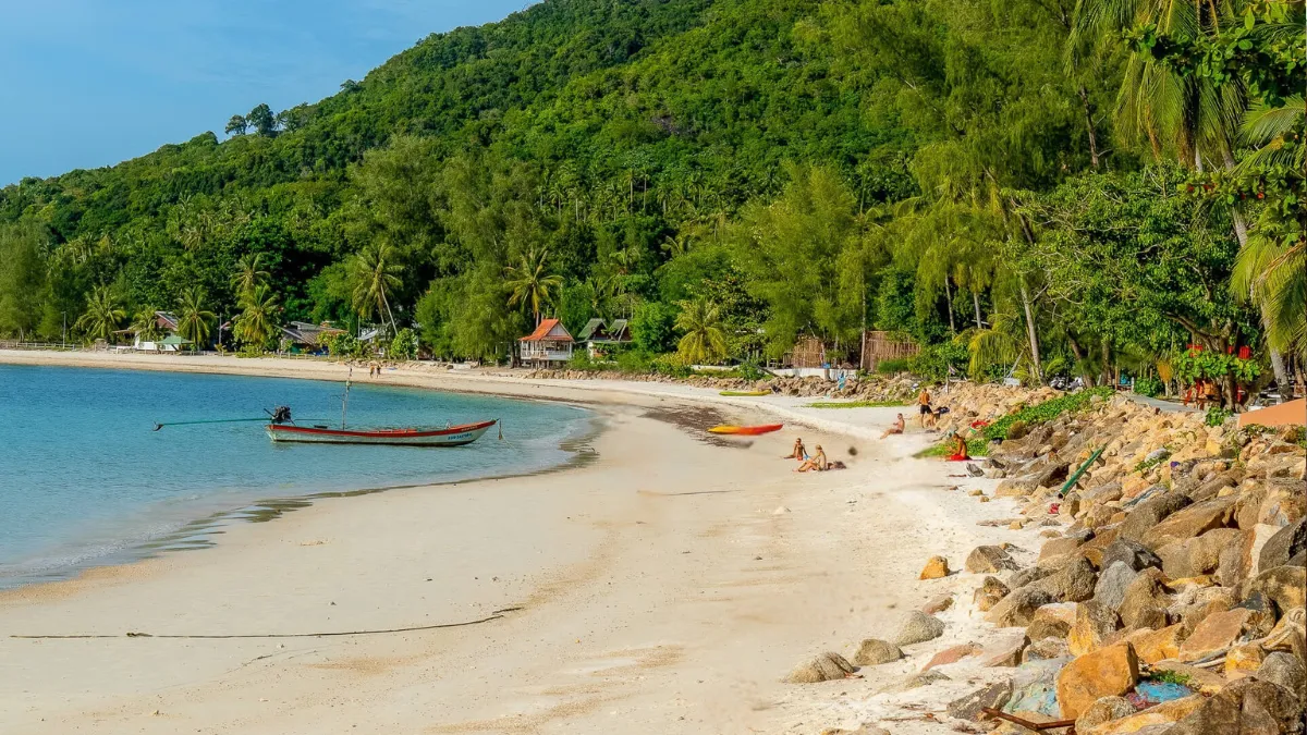 Tropical beach with a small boat in calm water, palm trees, and a green hillside behind it