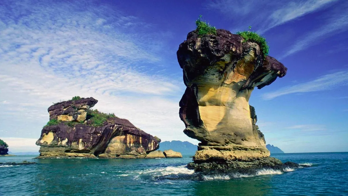 Two large sea stacks rising from blue ocean under a partly cloudy sky