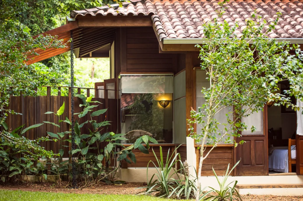 Wooden house with a tiled roof surrounded by lush tropical plants