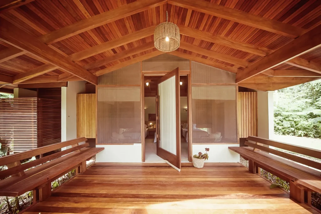 Wooden porch with a vaulted ceiling, benches, and an open door to a cabin interior