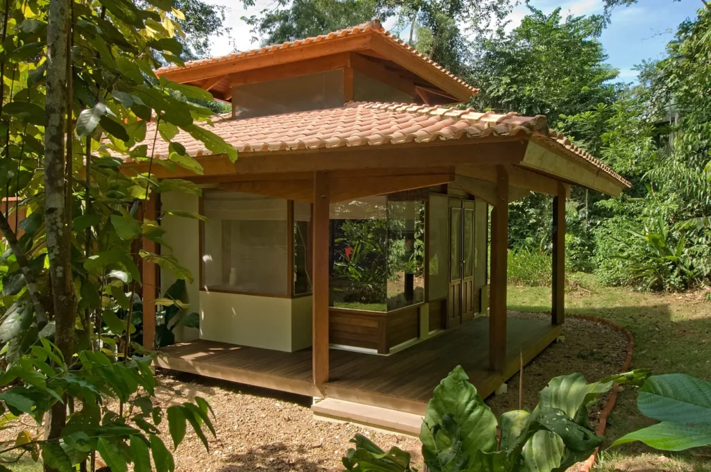 Small wooden house with a tiled roof surrounded by lush tropical greenery