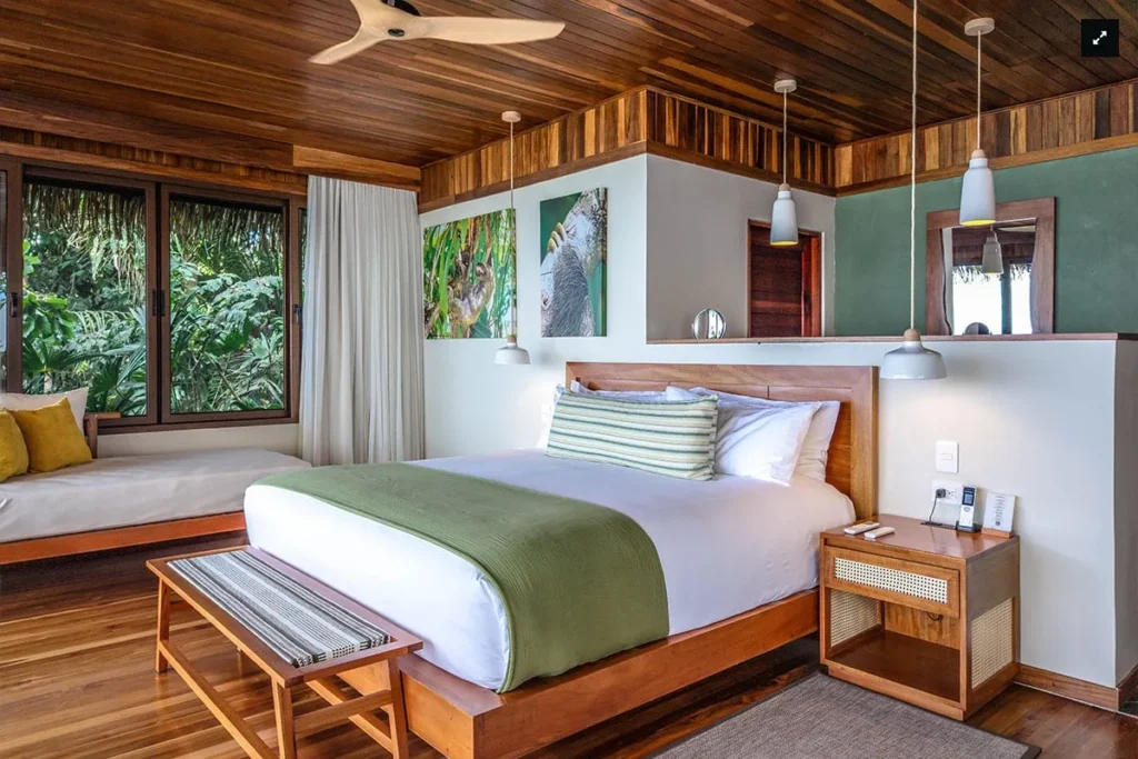 Tropical bedroom with a wooden bed, green bedding, and large windows overlooking lush greenery