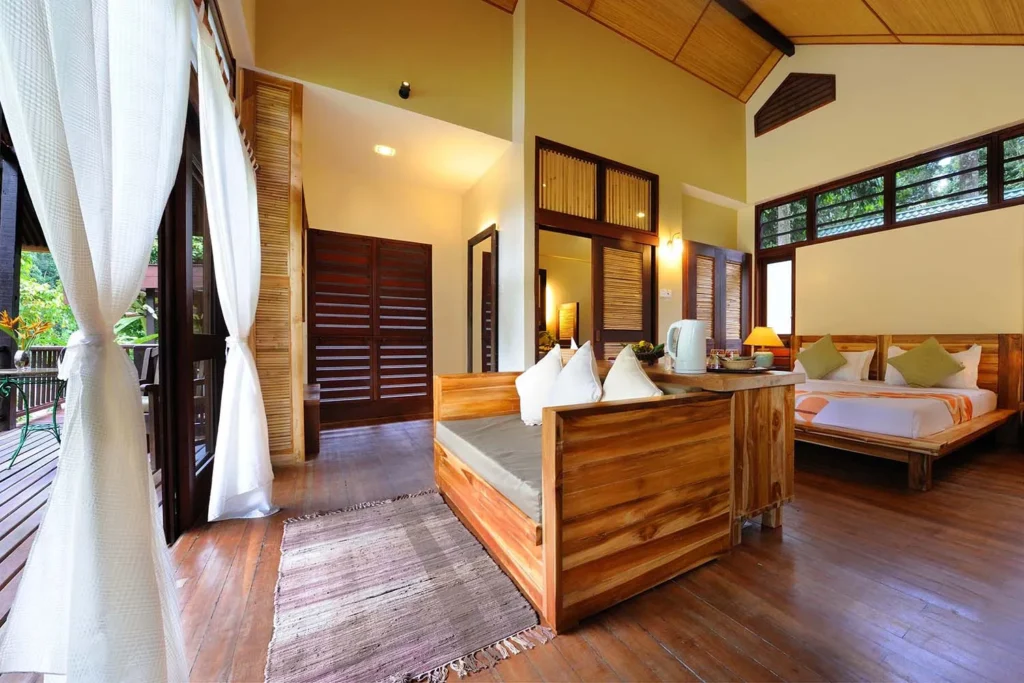 Spacious wooden bedroom with two beds, a seating area, and large windows overlooking a deck