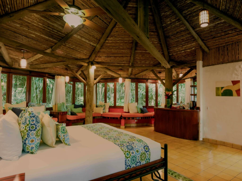 Open-air tropical bedroom with a canopy bed, lounge seating, and bamboo ceiling beams