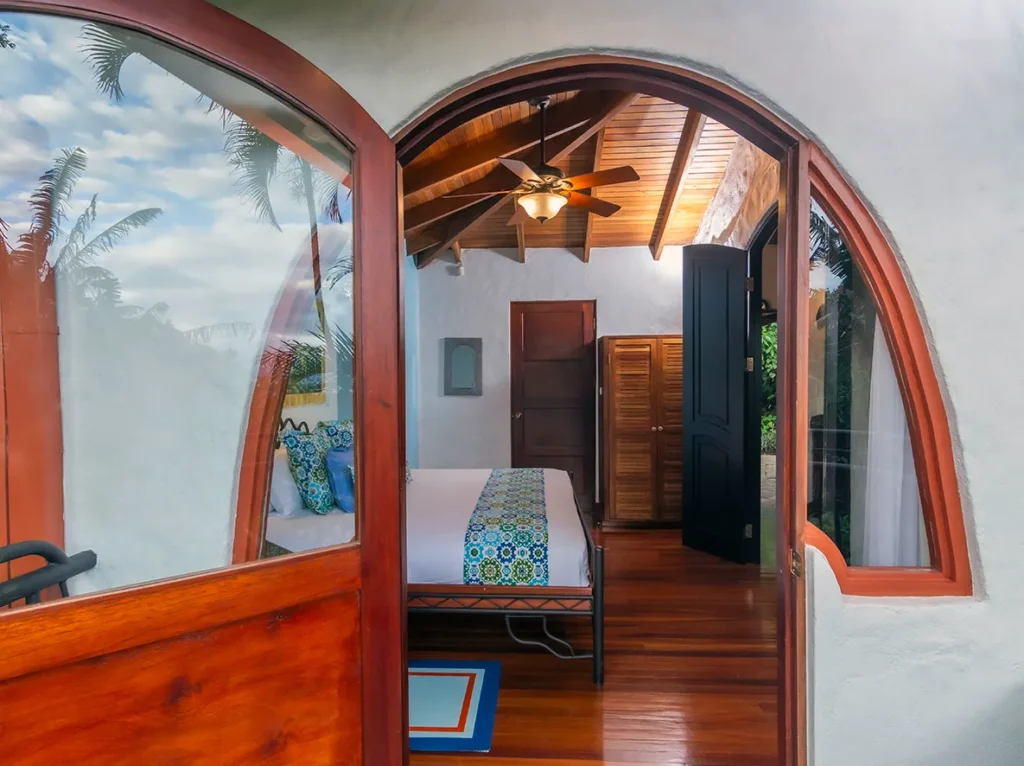 Bedroom with arched wooden doors, a ceiling fan, and tropical views through the windows