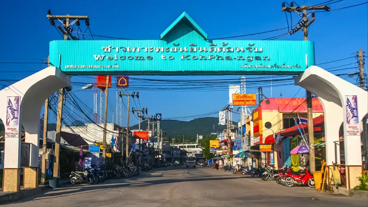 Welcome to Koh Phangan entrance arch over a street lined with shops and motorcycles