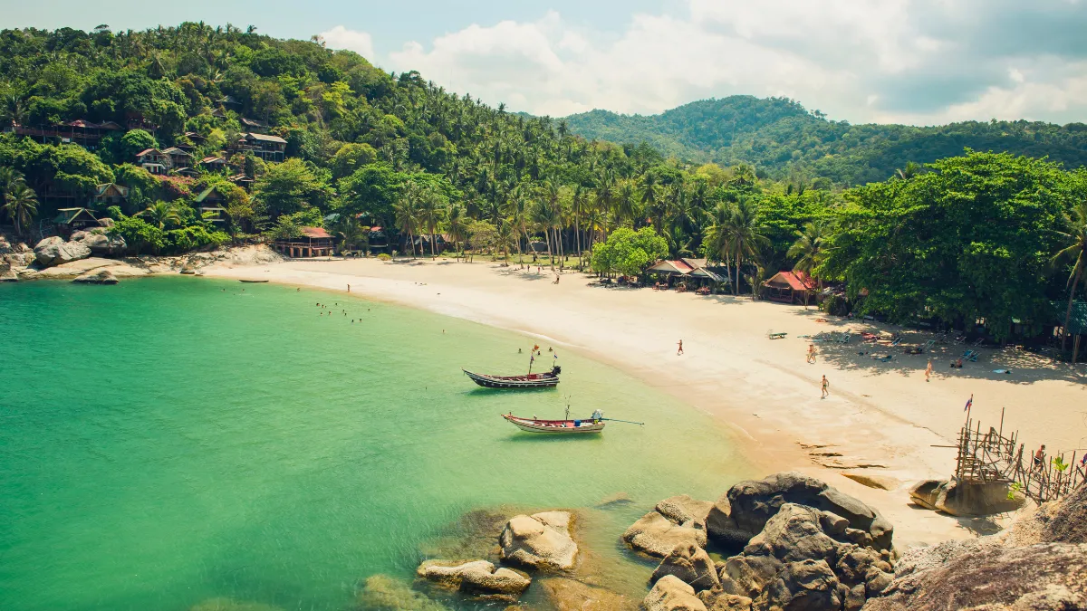 Tropical beach cove with clear green water, two boats, and palm-covered hills