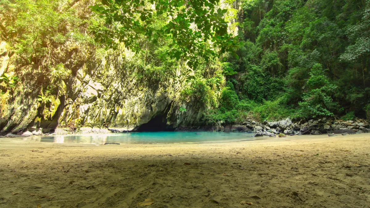 Secluded tropical cove with a sandy beach, turquoise water, and a cave beneath lush cliffs