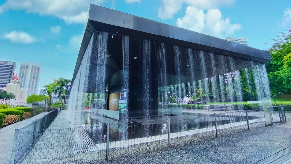 A modern pavilion with water curtains flowing down its sides in a park