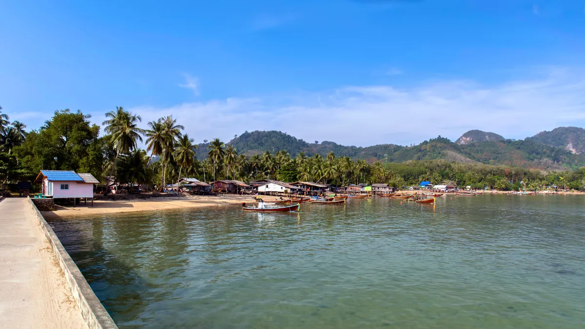 Tropical bay with fishing boats, palm trees, and mountains under a blue sky