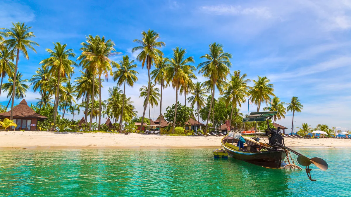 Tropical beach with palm trees and a long-tail boat in clear turquoise water