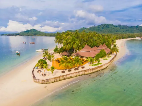 Aerial view of a tropical island resort with palm trees, beach, and overwater turquoise water