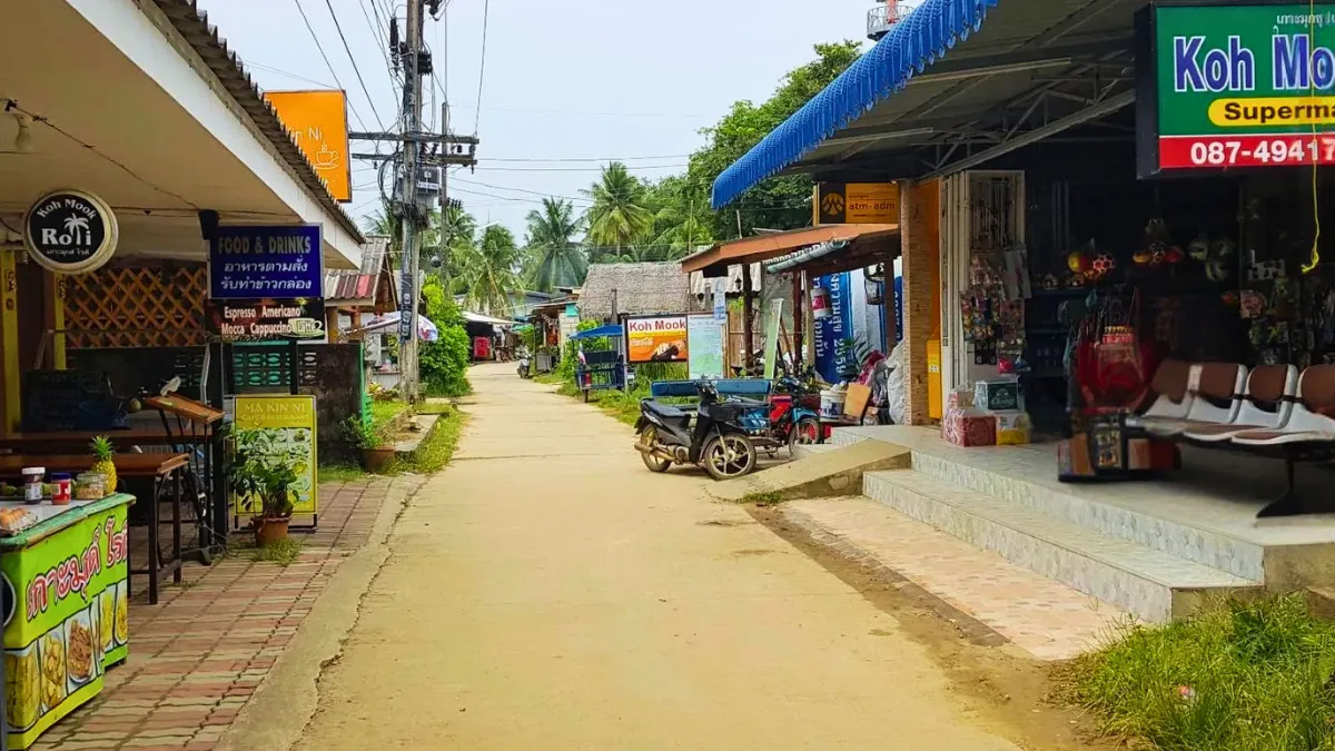 A small village street with shops, signs, and parked motorbikes under palm trees