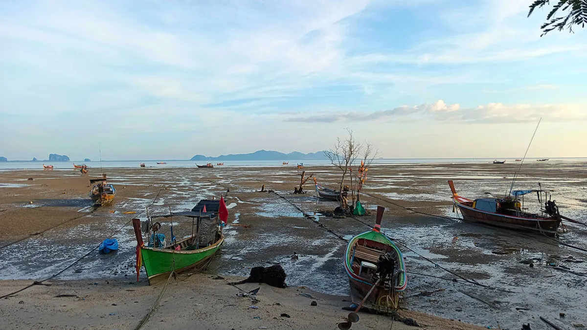 Fishing boats resting on a tidal flat at low tide under a cloudy sky