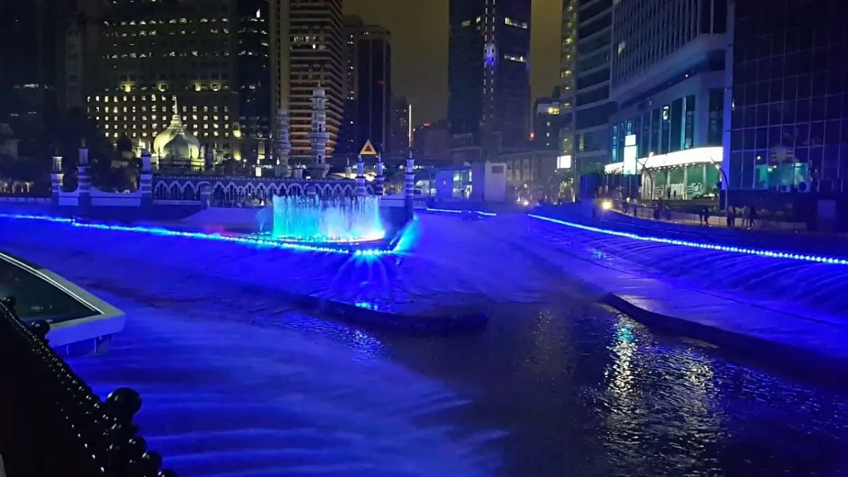 Nighttime city fountain lit in blue between tall buildings
