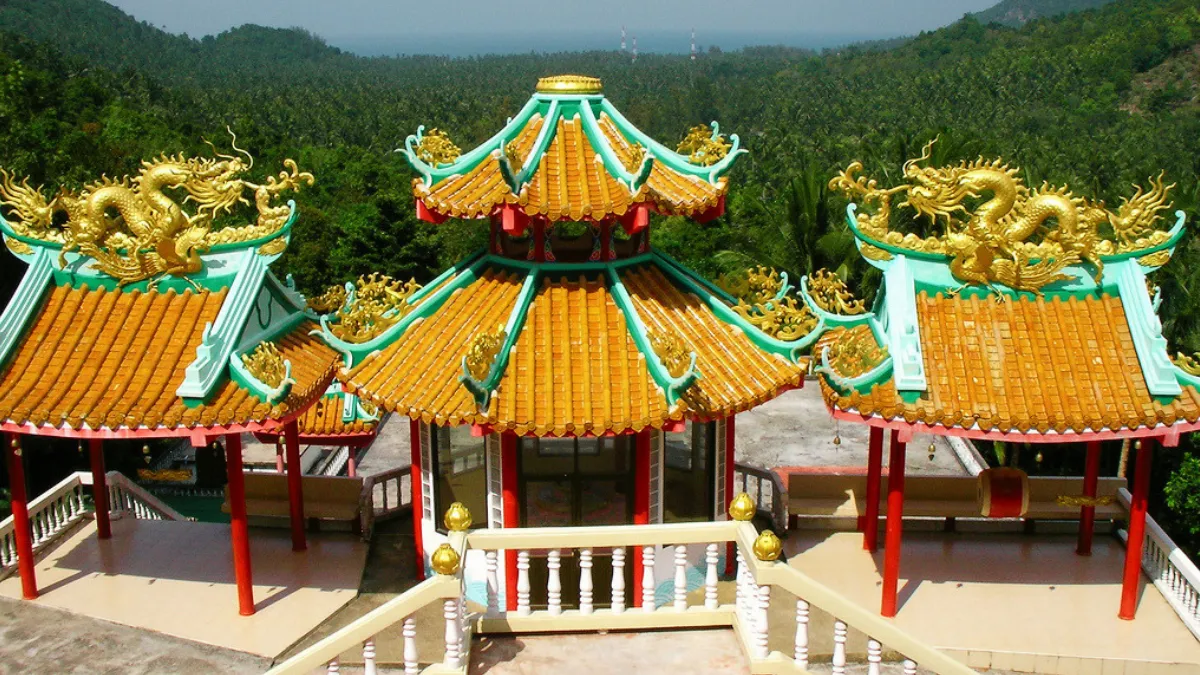 A colorful Chinese-style temple with golden dragon roof ornaments, set against forested hills