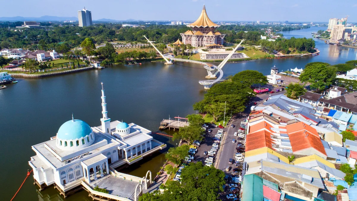 Aerial view of a riverside city with a blue-domed mosque, a landmark bridge, and a golden-roofed civic building