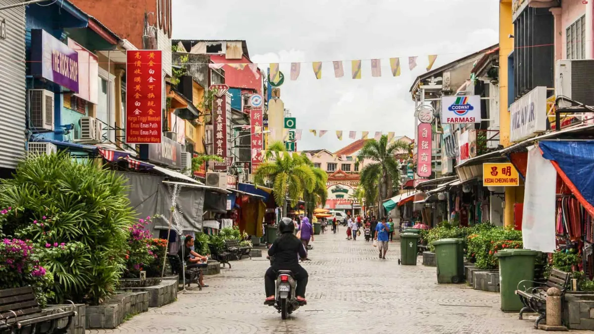 A colorful street lined with shops, signs, and pedestrians, with a motorbike riding down the center