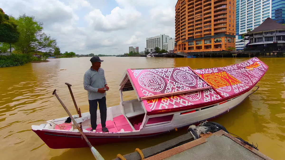 Man standing on a decorated boat on a river with city buildings in the background
