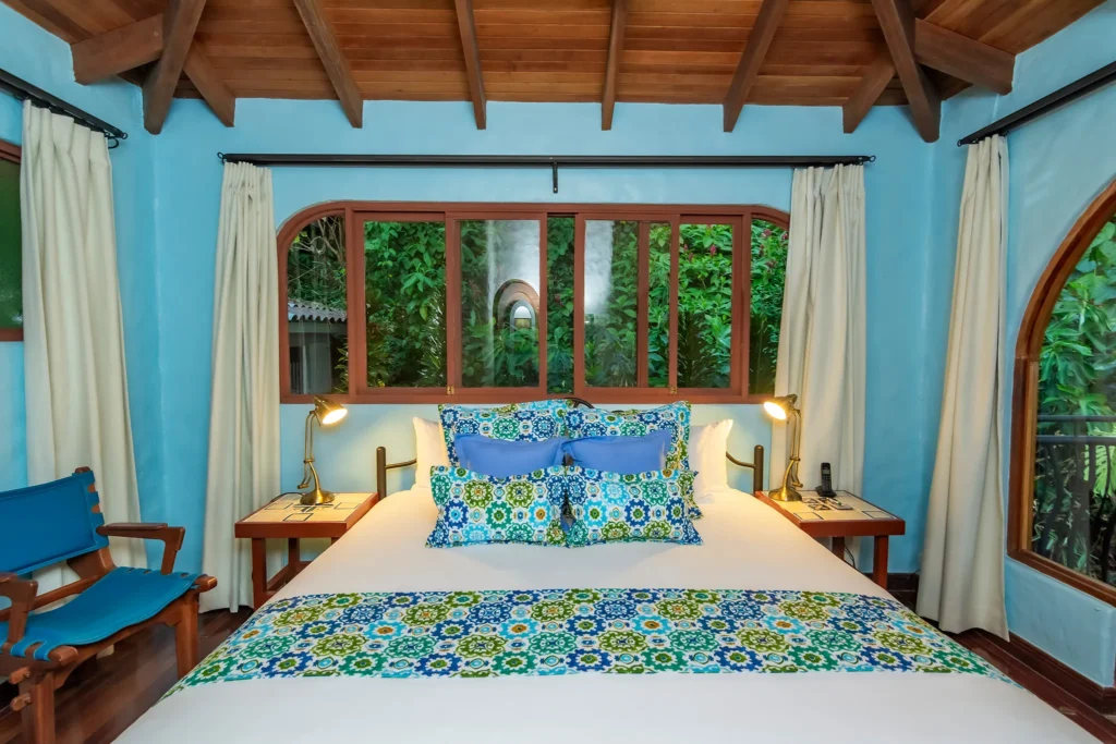 Bedroom with a bed, patterned bedding, bedside lamps, and large windows overlooking greenery