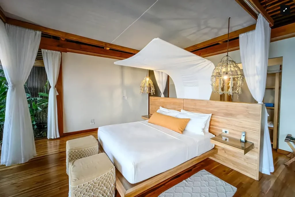 A modern bedroom with a canopy bed, white curtains, wooden accents, and hanging pendant lights
