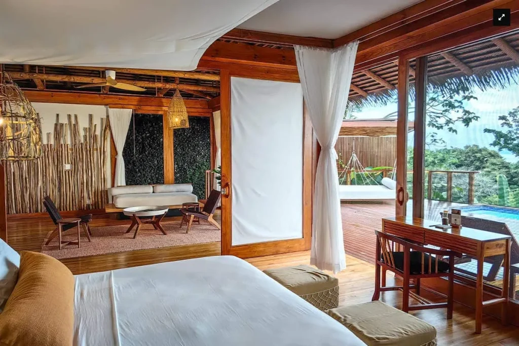 Luxury tropical villa bedroom with a sitting area, desk, and open view to a deck and pool