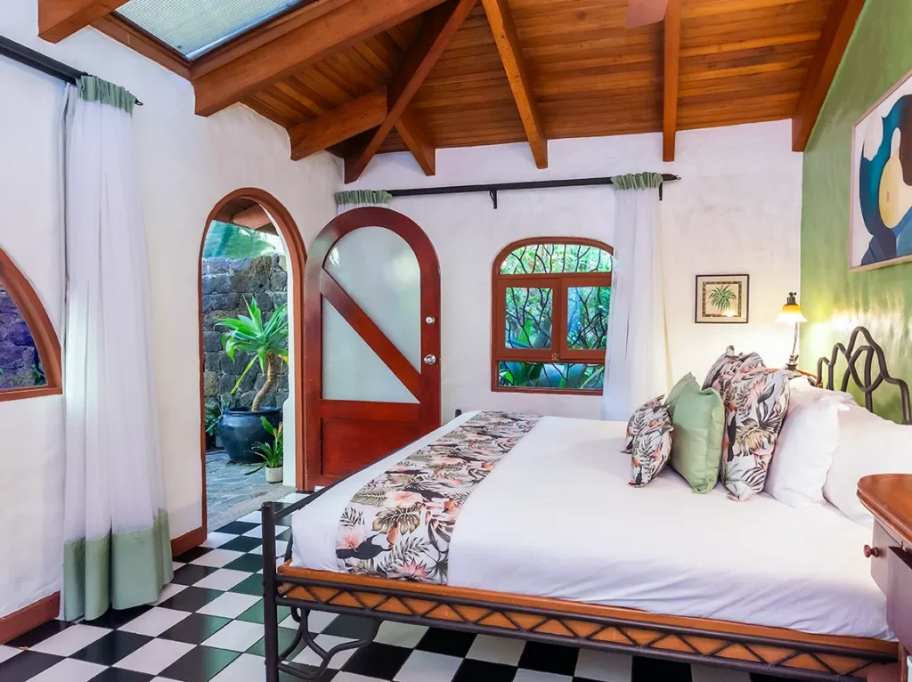 Bedroom with a wooden vaulted ceiling, checkered floor, and an open door to a garden patio