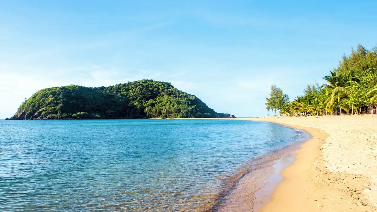 Tropical beach with calm blue water, a sandy shore, and a green island in the distance
