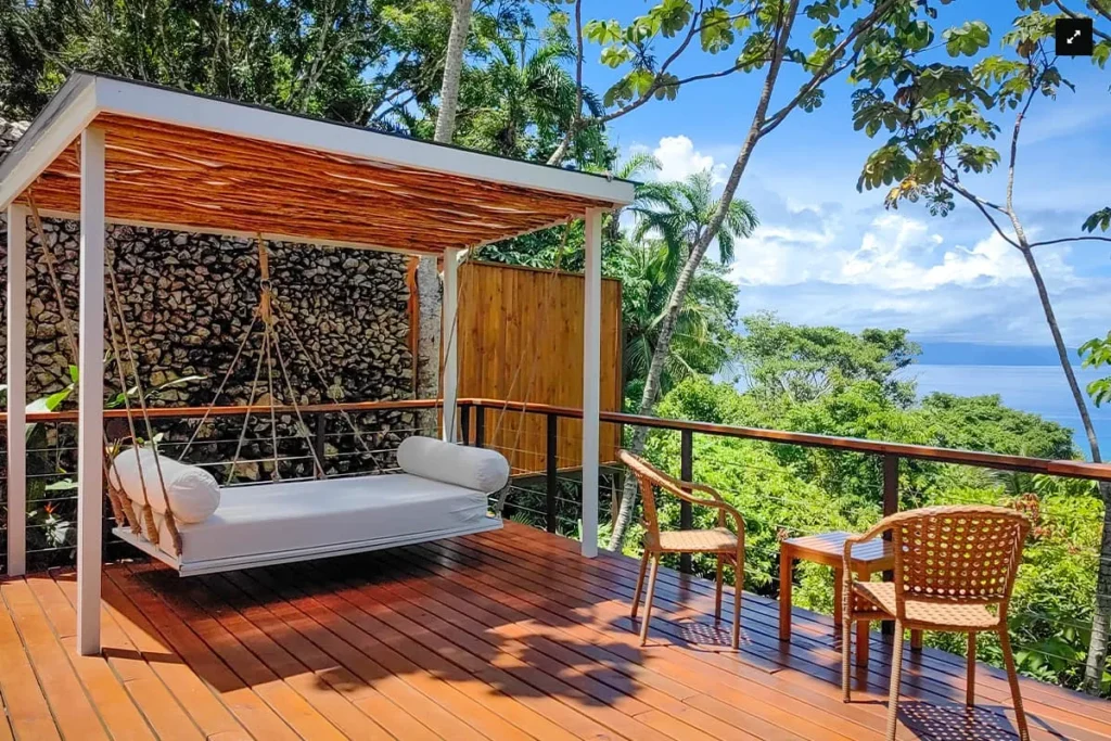 Covered deck with a hanging daybed and chairs overlooking a tropical ocean view