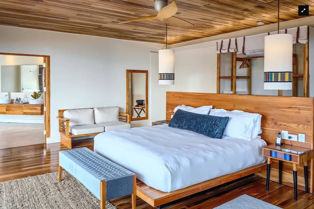 A modern bedroom with a wooden bed, bench, sofa, and pendant lights