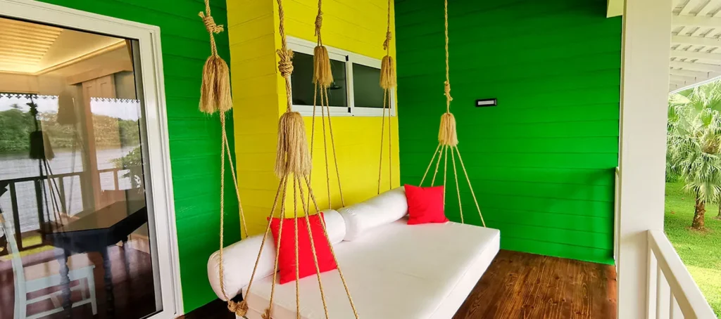 Porch swing daybed with white cushions and red pillows on a green and yellow porch