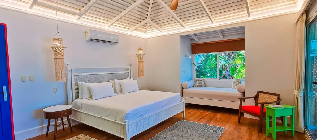 Bright bedroom with a white bed, window seat, and tropical garden view