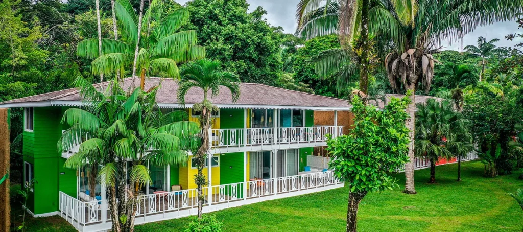 A green tropical resort building with balconies surrounded by palm trees and lush vegetation