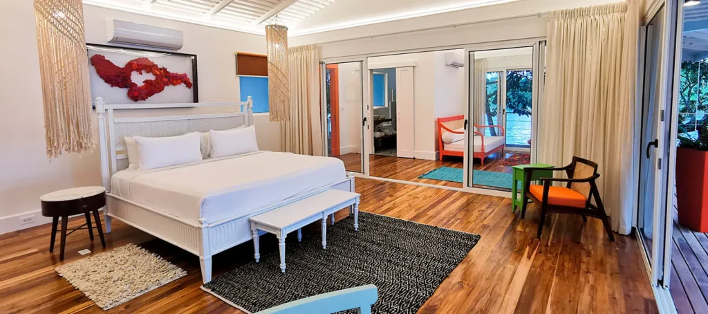 A bright bedroom with a white bed, mirrored closet doors, and a view of a patio through sliding glass doors