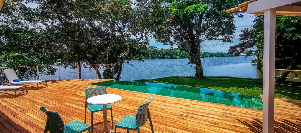 Lakefront deck with lounge chairs, a small table, and an infinity pool overlooking the water