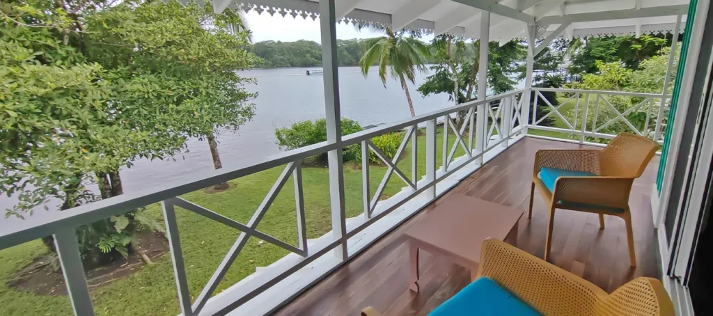 Covered balcony overlooking a tropical waterfront with chairs and a small table