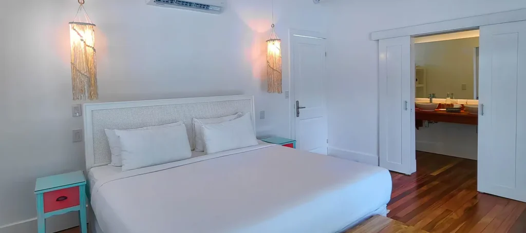 Bright bedroom with a white bed, hanging lamps, and an open doorway to a bathroom