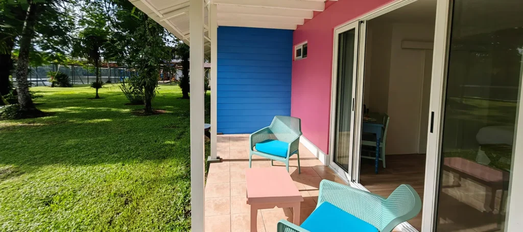 Patio with two turquoise chairs and a small table beside a colorful house, overlooking a grassy yard