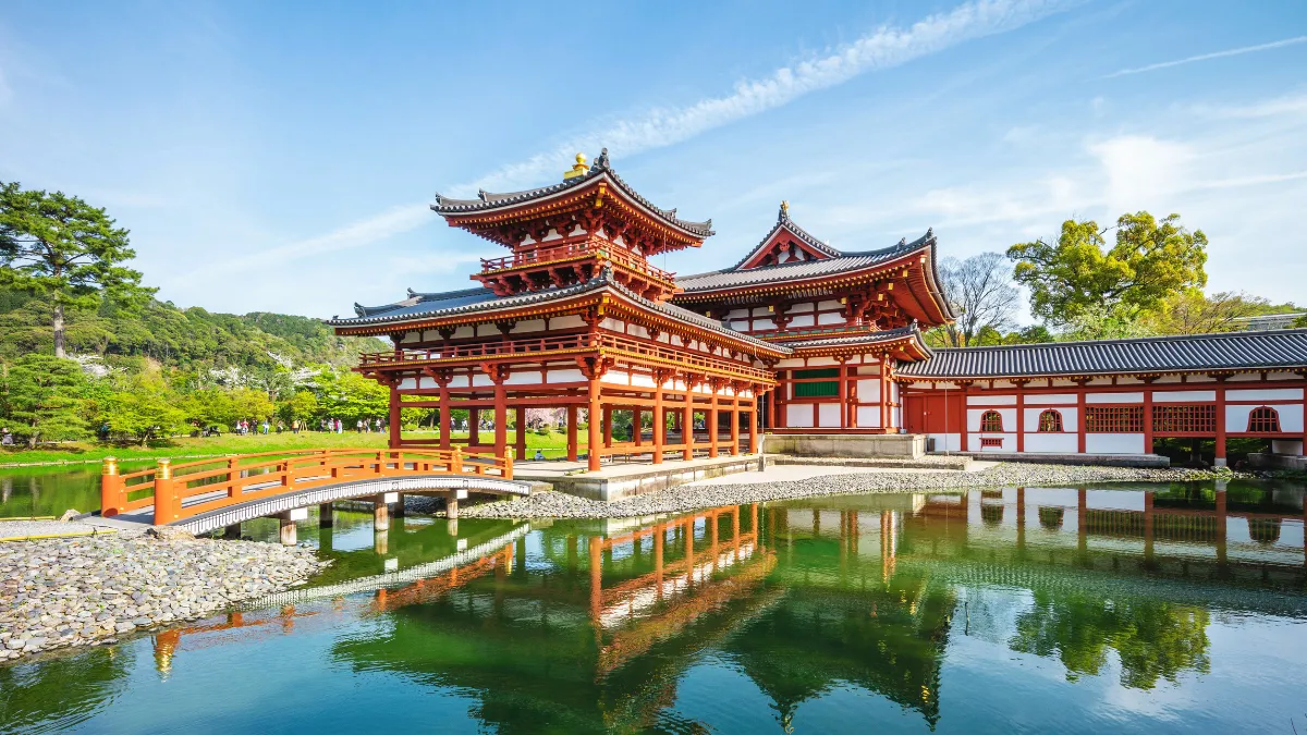 A Japanese temple pavilion with a red bridge reflected in a pond