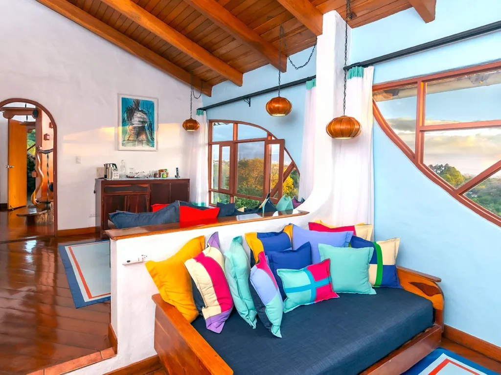 Colorful living room with wooden ceiling, hanging lights, and large windows overlooking a scenic view