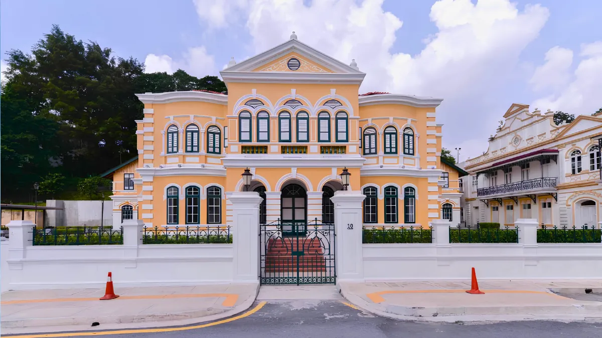 Historic pastel-yellow colonial-style building behind a white fence and gate
